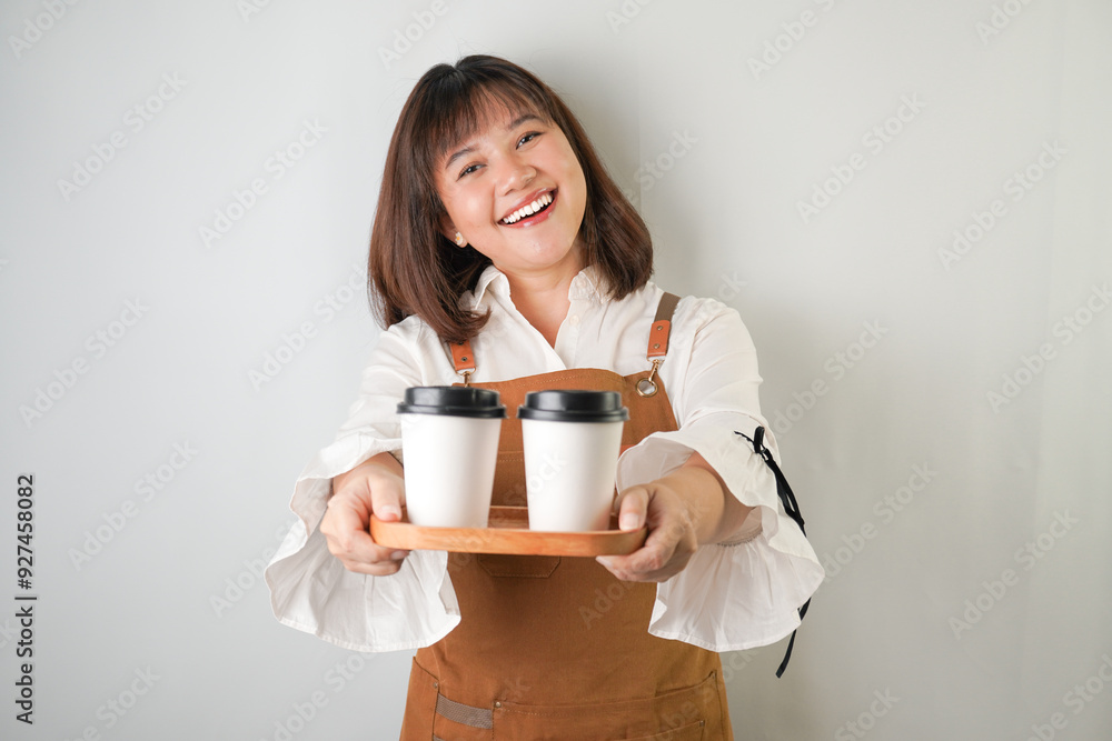 Excited young asian woman wearing long white sleeve shirt and brown apron is holding and serving coffee drinks to customer with smiling face expression. Isolated over white background. Excited young asian woman wearing long white sleeve shirt and brown apron is holding and serving coffee drinks to customer with smiling face expression. Isolated over white background.