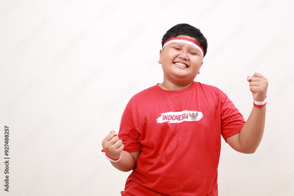 Fototapeta premium Young Asian boy with positive expression, joyful and exciting, dressed in casual cloth and red white ribbon over white background. Happy adorable glad boy rejoices success. Independence day concept