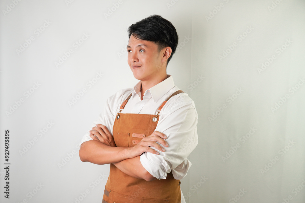Confident young asian man wearing rolled-up white sleeve shirt and brown apron is smiling face expression to camera with arms crossed hand gesture. Isolated over white background. Confident young asian man wearing rolled-up white sleeve shirt and brown apron is smiling face expression to camera with arms crossed hand gesture. Isolated over white background.