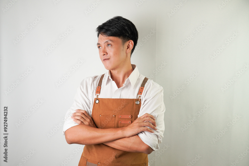 Confident young asian man wearing rolled-up white sleeve shirt and brown apron is smiling face expression to camera with arms crossed hand gesture. Isolated over white background. Confident young asian man wearing rolled-up white sleeve shirt and brown apron is smiling face expression to camera with arms crossed hand gesture. Isolated over white background.