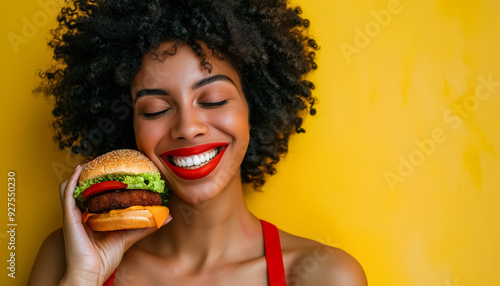Wallpaper Mural A woman is holding a hamburger and smiling. The hamburger is on a yellow background. The woman's expression is happy and joyful Torontodigital.ca