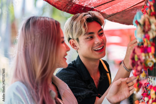 happy asian tourist couple buy items from local shop on vacation. cheerful boy and girl lover purchasing traditional gift shop on holiday. smiling female traveler checking crafting accessories to buy photo