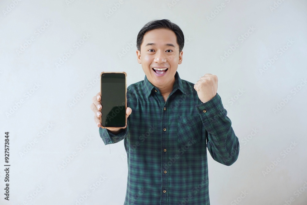 Adult Asian man in green long sleeve flannel shirt holding and showing smartphone display with black screen to camera with right hand while left hand making fist. Happy and cheerful expression. Adult Asian man in green long sleeve flannel shirt holding and showing smartphone display with black screen to camera with right hand while left hand making fist. Happy and cheerful expression.