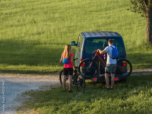 Young man is unloading electric mountain bikes, for himself and his girlfriend, lifting them from the hitch rack on the vehicle. photo