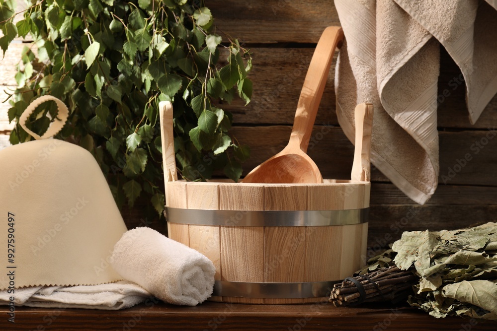 Sauna equipment. Bucket with ladle, felt wool hat, towels and whisks on wooden table indoors Sauna equipment. Bucket with ladle, felt wool hat, towels and whisks on wooden table indoors