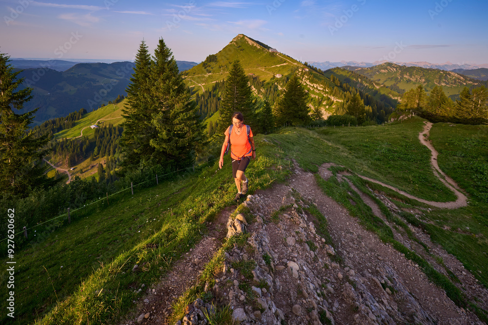 Naklejka premium pretty senior woman hiking in warm dawn sunlight and enjoying the spectacular view over the Allgau alps on the Nagelfluh mountain chain near Oberstaufen, Bavaria, Germany