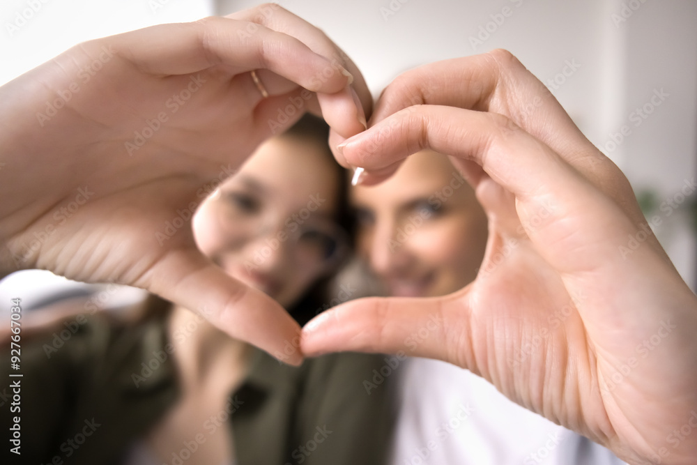 Fototapeta premium Close up face of teenager daughter and mother looking at camera, show symbol of love, demonstrate care and tenderness, enjoy time together at home, express support in family relationships. Bond, ties