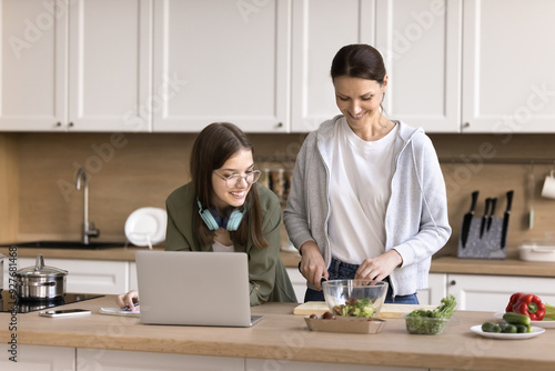 Photography Teen studying in kitchen while her smiling mother prepare lunch for family, lead friendly talk, advising her about essay theme, help with task