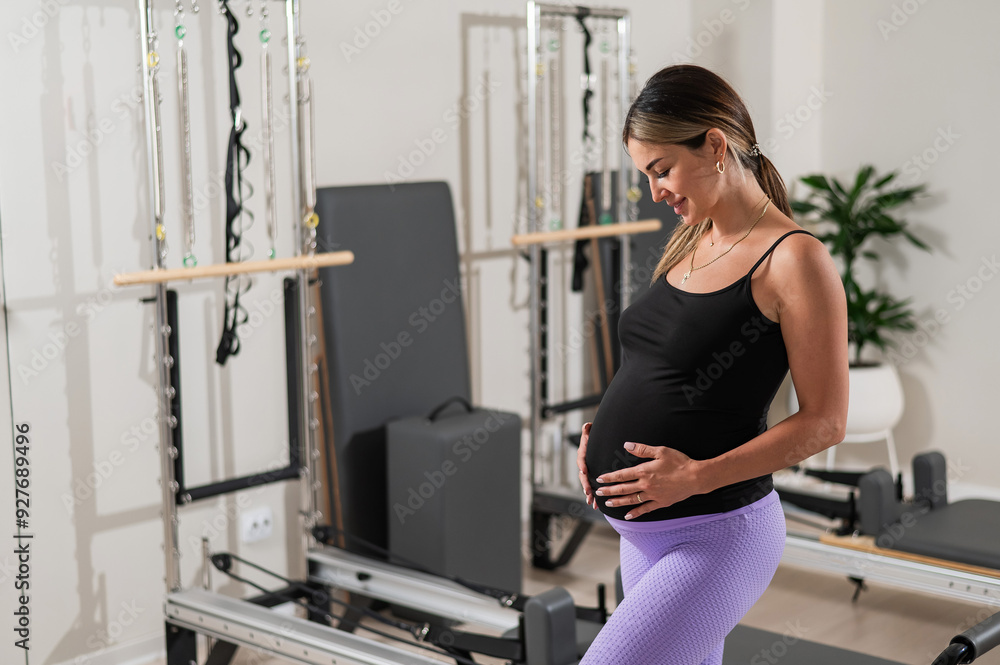 Beautiful pregnant woman stands in a yoga studio and gently touches her belly. Beautiful pregnant woman stands in a yoga studio and gently touches her belly.