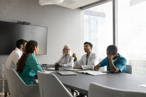 Indian male therapist wear white coat makes speech at group meeting medical seminar in modern conference room. Multiethnic clinic staff members listening opinion, decisions and solutions of workmate photo