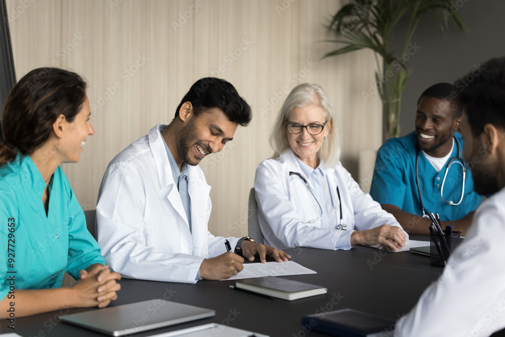 Smiling Indian male doctor put signature on legal document during meeting with group of diverse colleagues, approving treatment strategy for patient, hiring new specialist, signing employment contract Smiling Indian male doctor put signature on legal document during meeting with group of diverse colleagues, approving treatment strategy for patient, hiring new specialist, signing employment contract