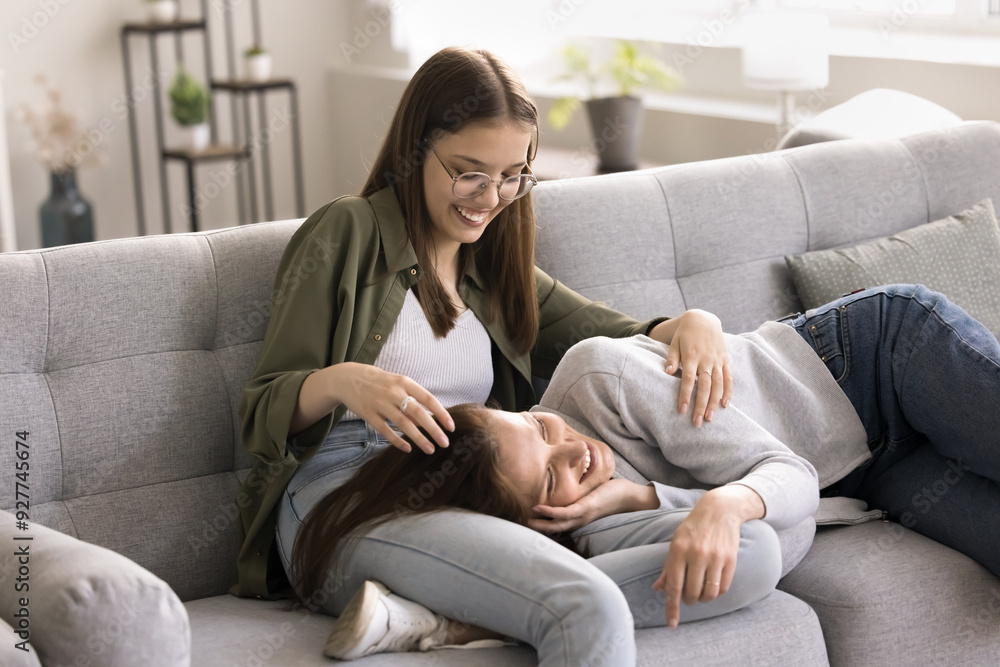 Fototapeta premium Loving teenager daughter strokes her mommy head with love attentively listening, share day news having good strong trustworthy relationships relaxing on weekend together on cozy sofa in living room