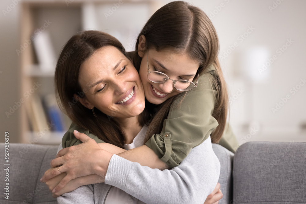 Loving smiling teenage girl hugs from behind mature mom, express love and care, enjoy family weekend at home, congratulate with Mothers Day, close up. Two gen relative people warm harmonic relations Loving smiling teenage girl hugs from behind mature mom, express love and care, enjoy family weekend at home, congratulate with Mothers Day, close up. Two gen relative people warm harmonic relations