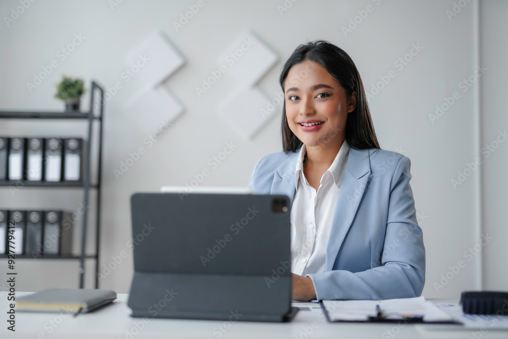 Young asian businesswoman smiling while working on a digital tablet in her bright modern office Young asian businesswoman smiling while working on a digital tablet in her bright modern office