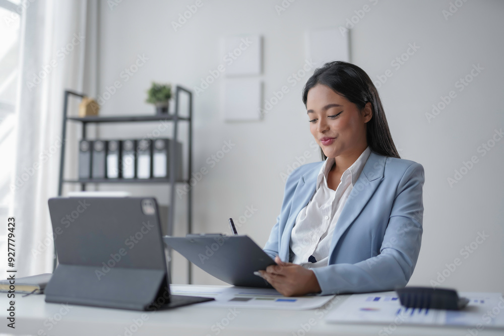 Businesswoman is reviewing documents at her desk and smiling with a tablet computer next to her Businesswoman is reviewing documents at her desk and smiling with a tablet computer next to her