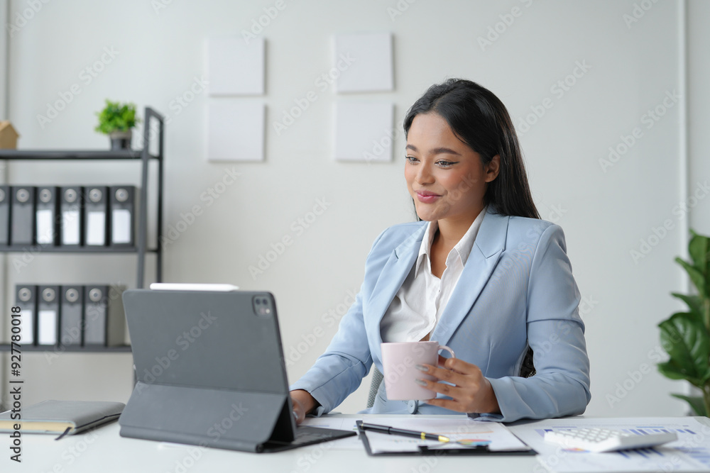 Businesswoman working from her office, using a tablet and enjoying a cup of coffee Businesswoman working from her office, using a tablet and enjoying a cup of coffee