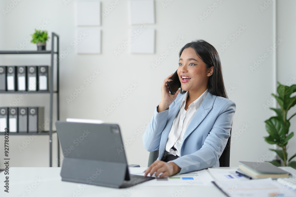 Businesswoman is multitasking in her office, smiling while talking on the phone and using her tablet Businesswoman is multitasking in her office, smiling while talking on the phone and using her tablet