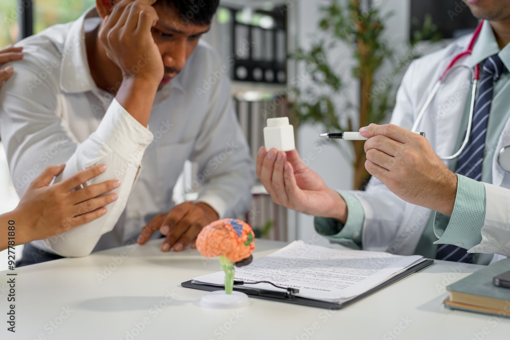 Doctor is explaining a treatment based on pills to a male patient experiencing a headache while his wife is comforting him Doctor is explaining a treatment based on pills to a male patient experiencing a headache while his wife is comforting him