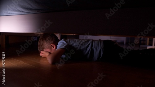 Scared child hiding under the bed at night
