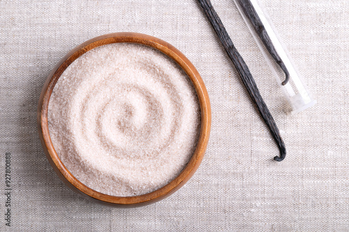 Vanilla sugar, flavored sugar in a wooden bowl on linen fabric, next to dried, brown, ripe pods or beans of Vanilla planifolia, a spice with distinctive flavor, used for baking and food flavoring. photo