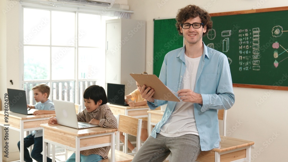 Caucasian teacher checking document and looking at camera at classroom. Diverse children sitting at learning about coding engineering prompt and generated AI. Cute student programing system. Pedagogy. Caucasian teacher checking document and looking at camera at classroom. Diverse children sitting at learning about coding engineering prompt and generated AI. Cute student programing system. Pedagogy.