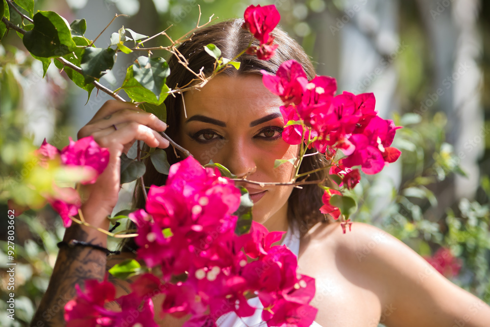 Fototapeta premium Portrait of young woman, brunette, beautiful, very tattooed, with white top, looking through bougainvilleas. Concept tattoos, nonconformism, rebel, trend, flowers.