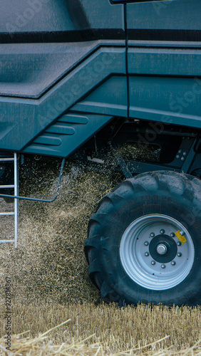 Obraz na płótnie Side view of a combine harvester in a wheat field, focusing on the machinery's tire and chaff dispersion. Advanced farming technology during harvest season. Agricultural efficiency. Vertical photo w salonie