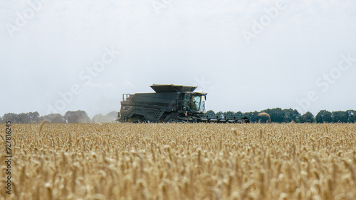 Obraz na płótnie Combine harvester in a wheat field, mid-distance view, capturing the harvesting process. Efficient agricultural machinery working during harvest season. Farming technology in action. w salonie