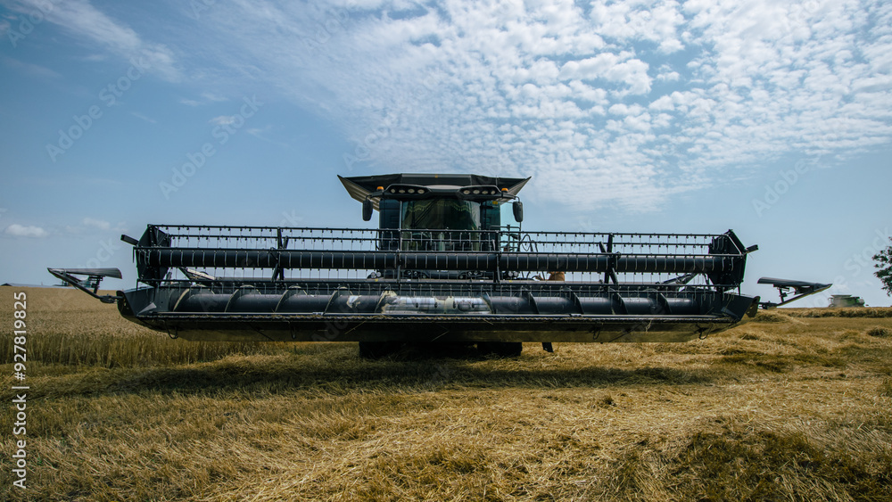 Front view of a combine harvester working in a wheat field under a bright sky. High-efficiency agricultural machinery in action during harvest season. Farming technology and innovation.