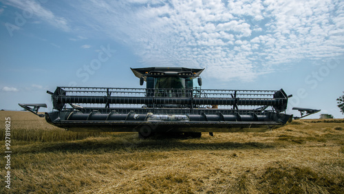 Obraz na płótnie Front view of a combine harvester working in a wheat field under a bright sky. High-efficiency agricultural machinery in action during harvest season. Farming technology and innovation. w salonie