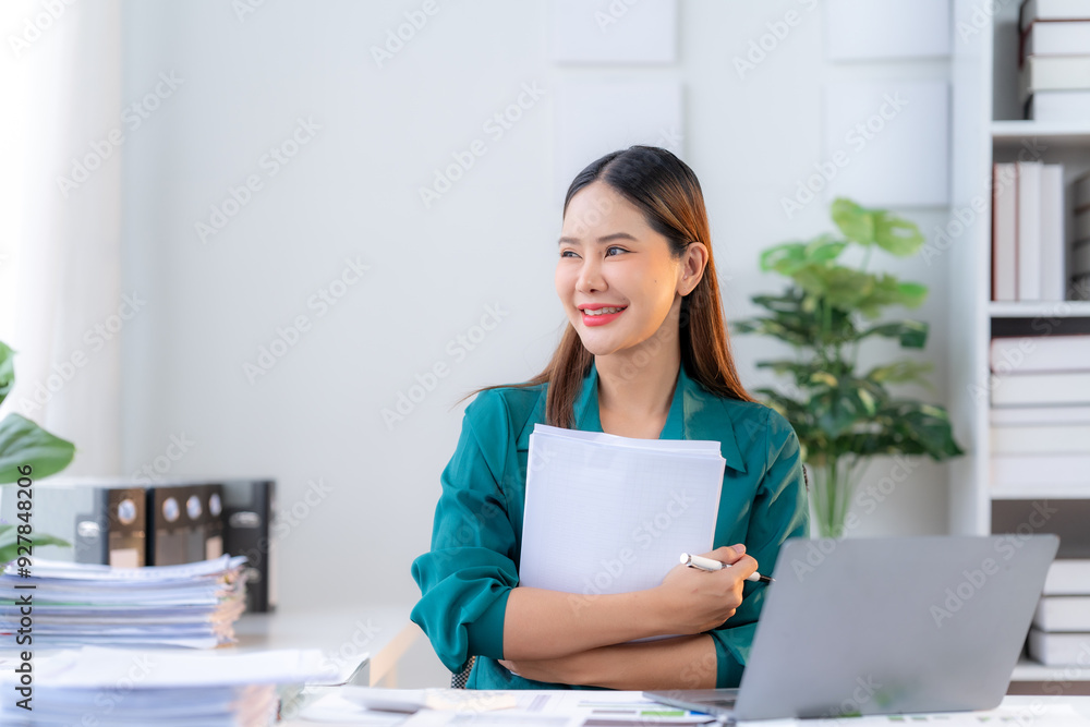 Confident Young Professional: A young Asian businesswoman exudes confidence as she reviews documents in her modern office, her gaze filled with ambition and optimism. Confident Young Professional: A young Asian businesswoman exudes confidence as she reviews documents in her modern office, her gaze filled with ambition and optimism.