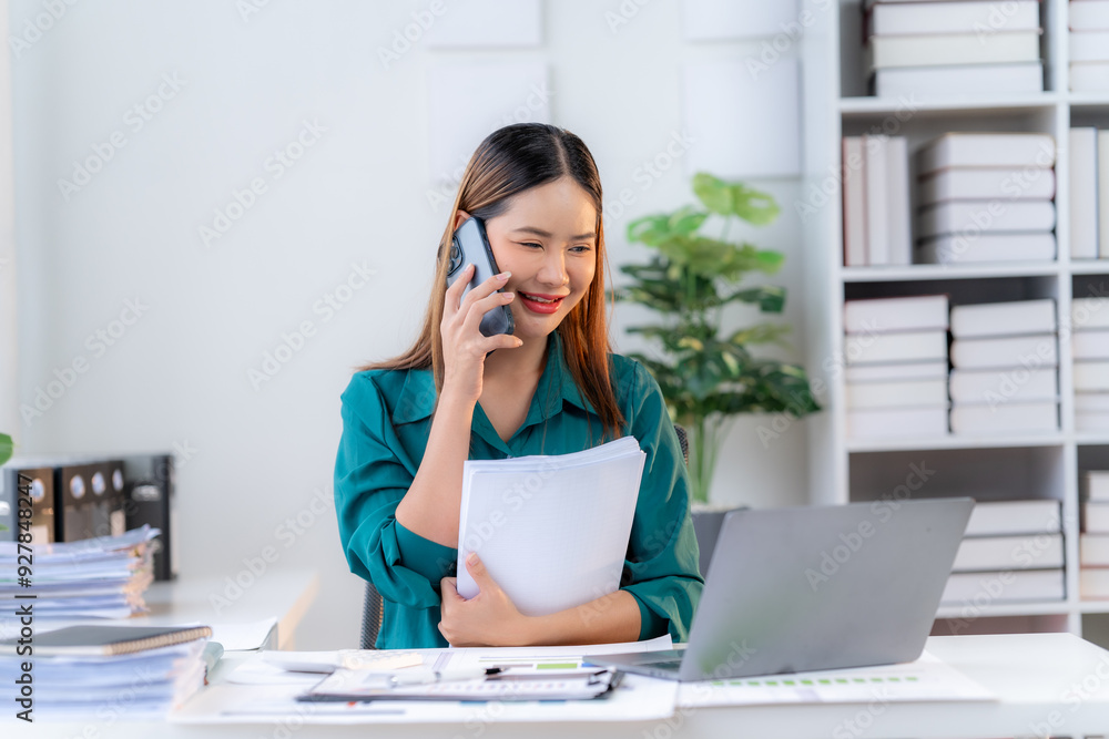 Confident Businesswoman on the Phone: A professional woman, dressed in a stylish green blouse, sits at her desk, engrossed in a phone conversation. She holds a folder in one hand, exuding confidence a Confident Businesswoman on the Phone: A professional woman, dressed in a stylish green blouse, sits at her desk, engrossed in a phone conversation. She holds a folder in one hand, exuding confidence a