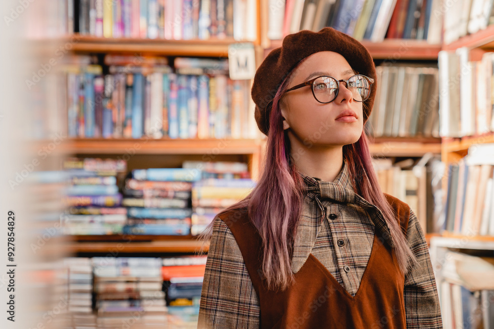 Dreamy thoughtful caucasian young hipster high school girl pupil student teenager in glasses standing in the university library or bookshop choosing the book for study exam homework Dreamy thoughtful caucasian young hipster high school girl pupil student teenager in glasses standing in the university library or bookshop choosing the book for study exam homework