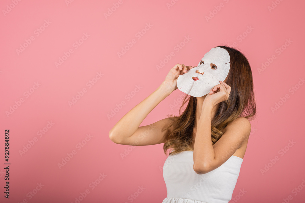 Portrait Asian young woman applying cosmetic paper sheet mask on her face studio shot isolated on pink background, beautiful female with natural makeup cosmetic mask, beauty skin care concept Portrait Asian young woman applying cosmetic paper sheet mask on her face studio shot isolated on pink background, beautiful female with natural makeup cosmetic mask, beauty skin care concept