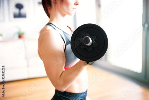 Beautiful redhead woman's home workout routine with dumbbell. Home fitness workout in living room, sporty woman wearing sportswear.