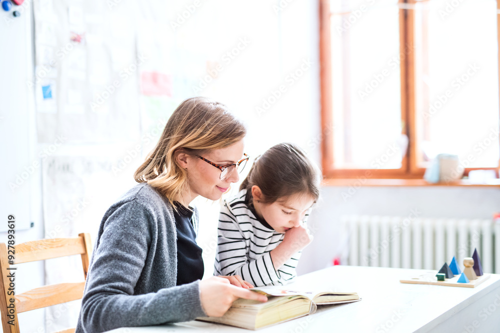 Hardworking teacher learning with young schoolgirl in classroom, helping with reading problem. Dyslexia. One to one lesson. Hardworking teacher learning with young schoolgirl in classroom, helping with reading problem. Dyslexia. One to one lesson.