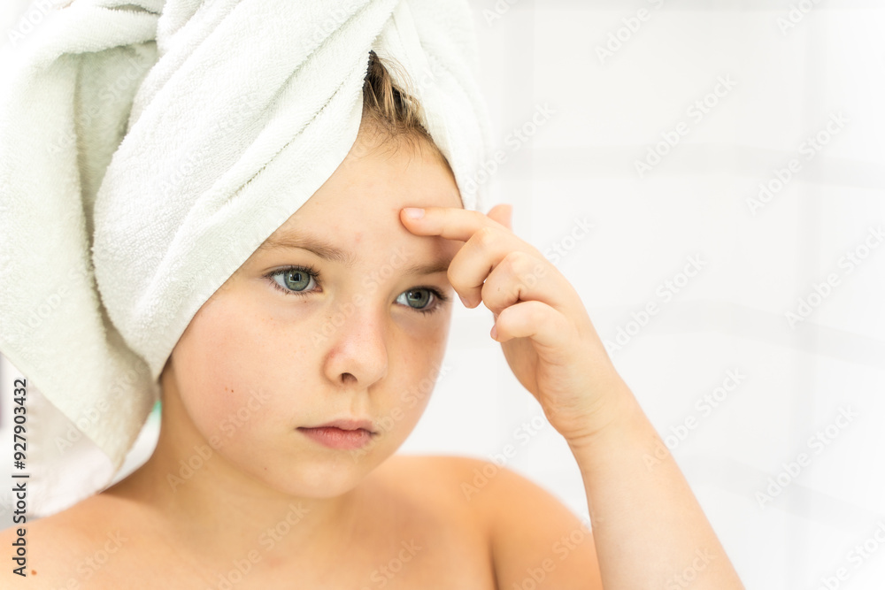 Little teenage girl in bath towel looking in mirror and pointing to acne. The concept of teenage skin problems. Puberty Little teenage girl in bath towel looking in mirror and pointing to acne. The concept of teenage skin problems. Puberty