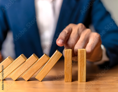 hand halts wooden dominoes from falling over, symbolizing the prevention of a business crisis and the control of potential disruptions photo