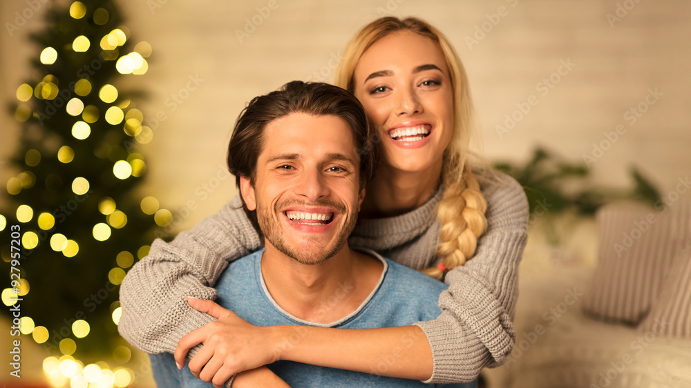 Happy couple looking at camera on new year's eve, woman embracing man in front of Christmas tree Happy couple looking at camera on new year's eve, woman embracing man in front of Christmas tree