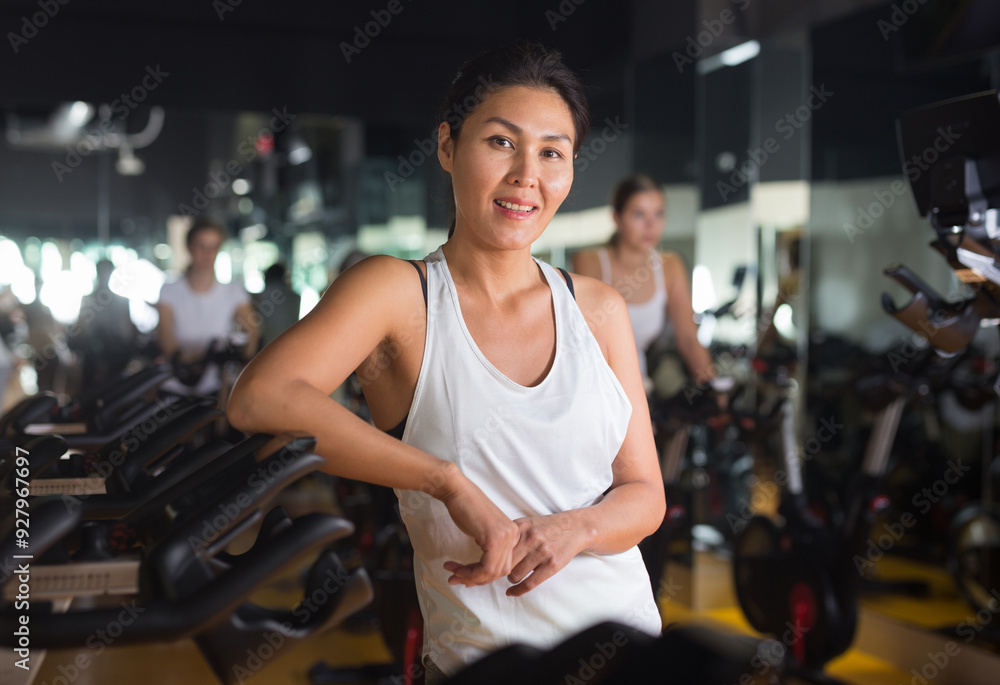 Fototapeta premium Portrait of confident asian woman posing near fitness bike in gym indoor