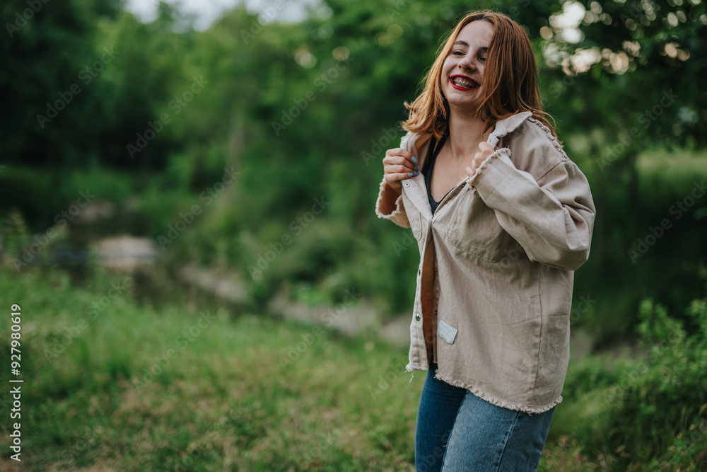 A joyful young woman with red hair smiles while enjoying a serene moment in a lush green outdoor environment. A joyful young woman with red hair smiles while enjoying a serene moment in a lush green outdoor environment.