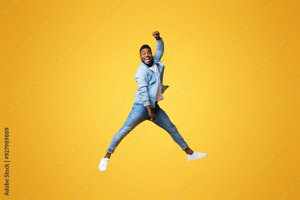 Full length of funny black guy jumping with raised arm against yellow studio background, copy space Full length of funny black guy jumping with raised arm against yellow studio background, copy space