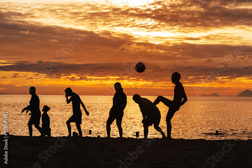 Silhouettes of Asian men ball players playing traditional beach soccer sepak takraw by the sea in summer at sunrise photo