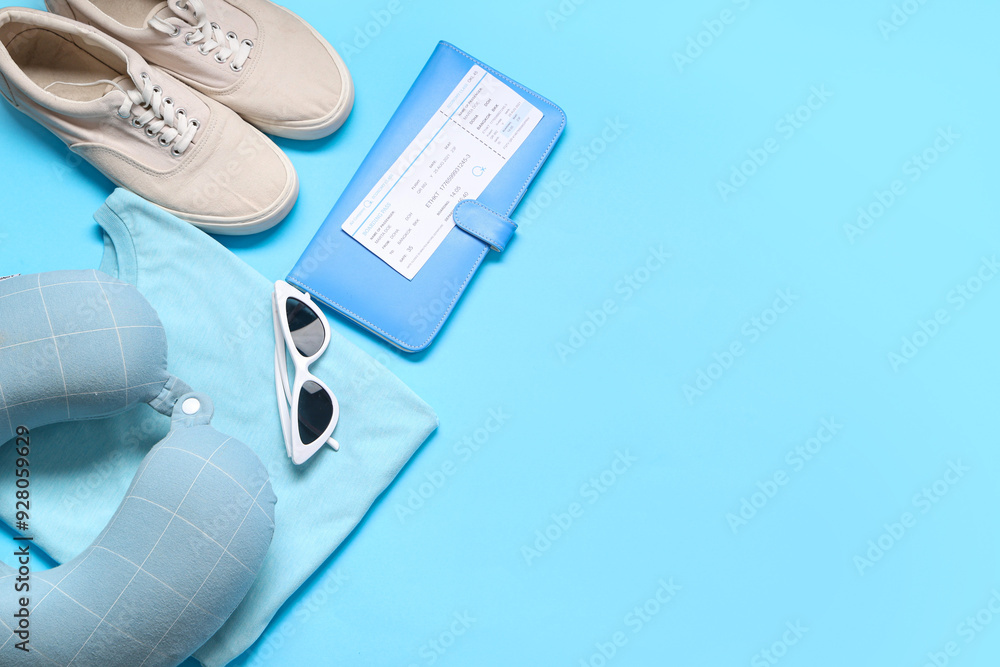 Travel pillow, wallet, ticket, t-shirt, sunglasses and shoes on blue background Travel pillow, wallet, ticket, t-shirt, sunglasses and shoes on blue background