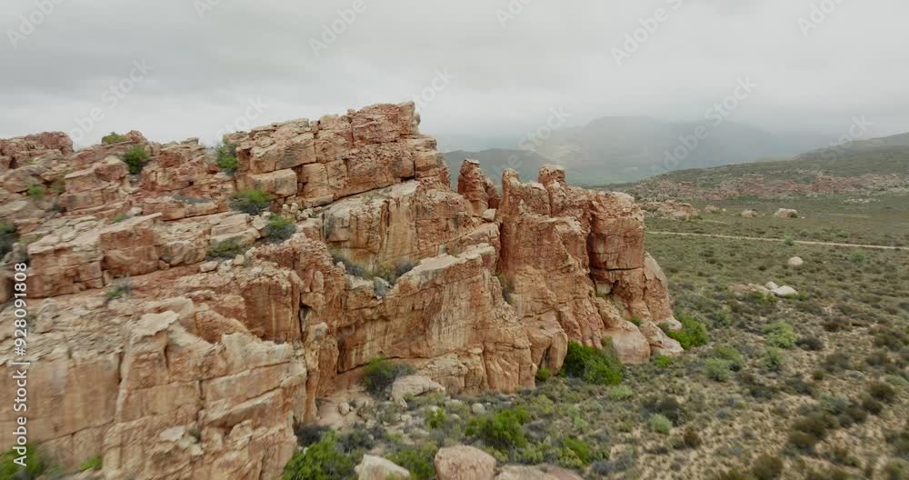 Drone flies quickly past a rock formation towards a road where a black off-road vehicle drives in the desert landscape in Cederberg Wilderness Area in South Africa - in the background are mountains Drone flies quickly past a rock formation towards a road where a black off-road vehicle drives in the desert landscape in Cederberg Wilderness Area in South Africa - in the background are mountains