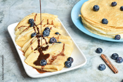 A serving of pancakes on a plate with blueberries and drizzled with chocolate glaze