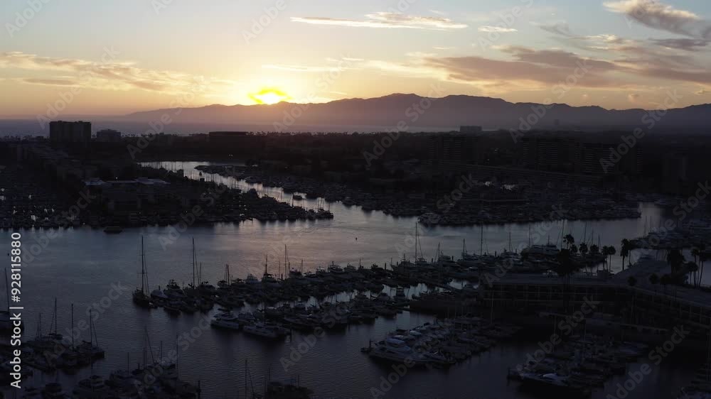 An aerial parallax shot of docked sailboats silhouetted against the sunset in Los Angeles, California An aerial parallax shot of docked sailboats silhouetted against the sunset in Los Angeles, California