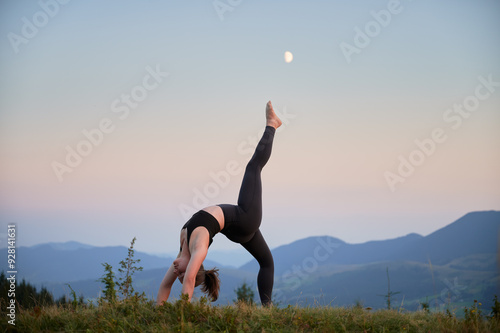 Woman practicing yoga outdoors in the mountains in a serene, natural setting. Female performing yoga pose, with backdrop of beautiful mountain landscape at sunrise or sunset. photo