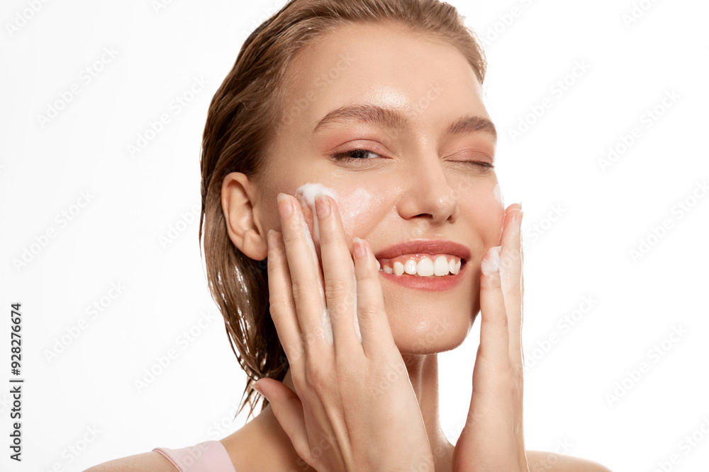 Smiling young woman applying cosmetic foam portrait. Cheerful laughing millennial girl washing on face looking at camera. Smiling young woman applying cosmetic foam portrait. Cheerful laughing millennial girl washing on face looking at camera.