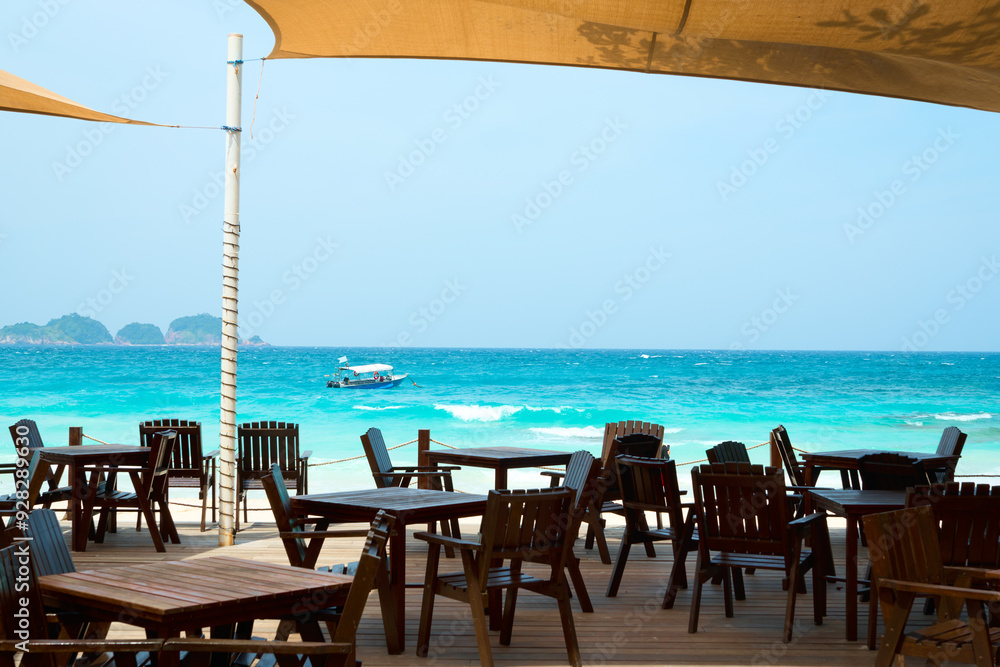 Fototapeta premium Empty wooden restaurant tables facing beautiful tropical ocean view